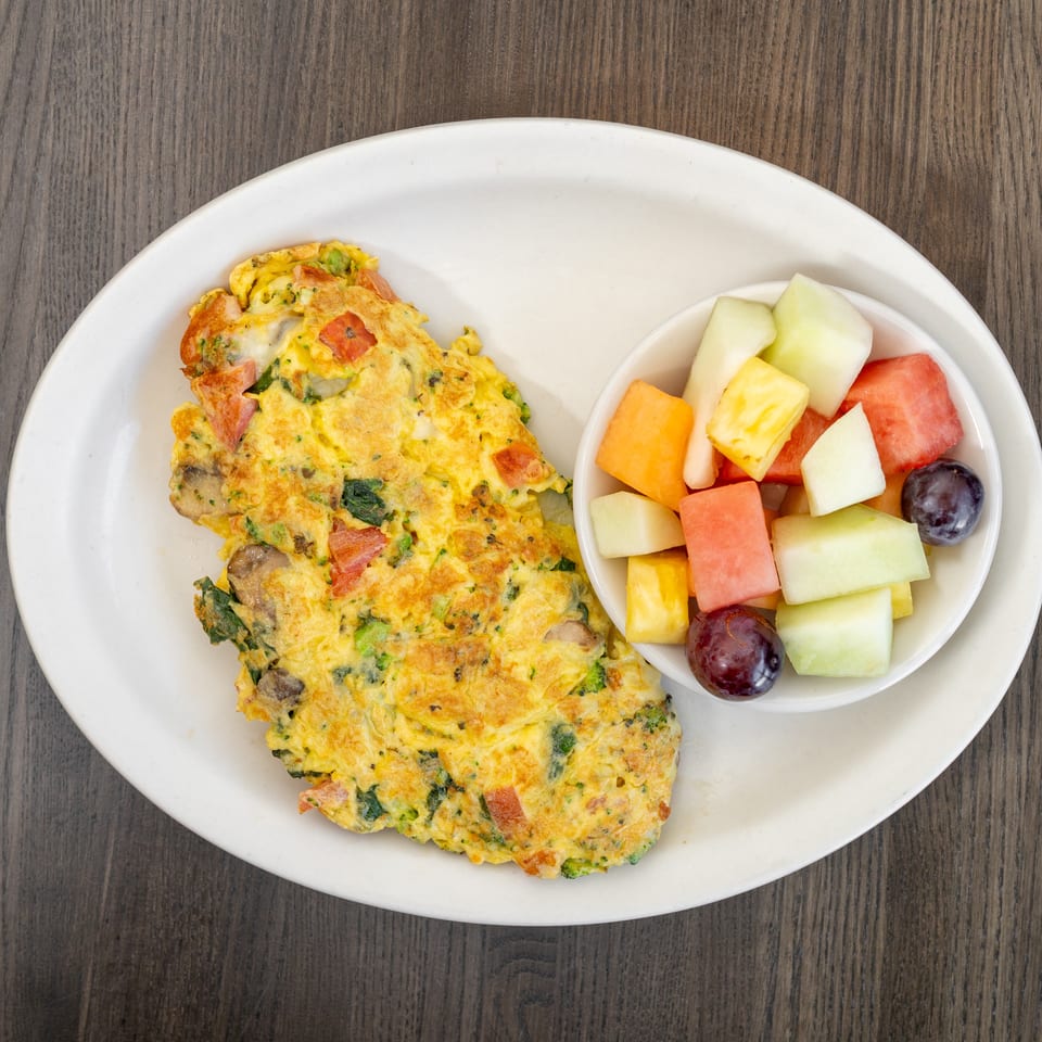 A vegetable omelet with mushrooms, broccoli, and tomatoes, served with a side of fresh fruit.