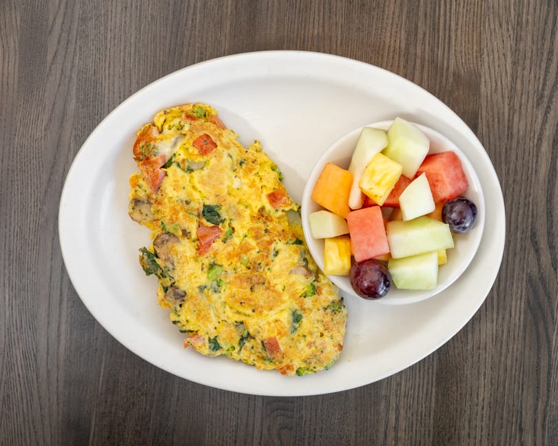 A vegetable omelet with mushrooms, broccoli, and tomatoes, served with a side of fresh fruit.