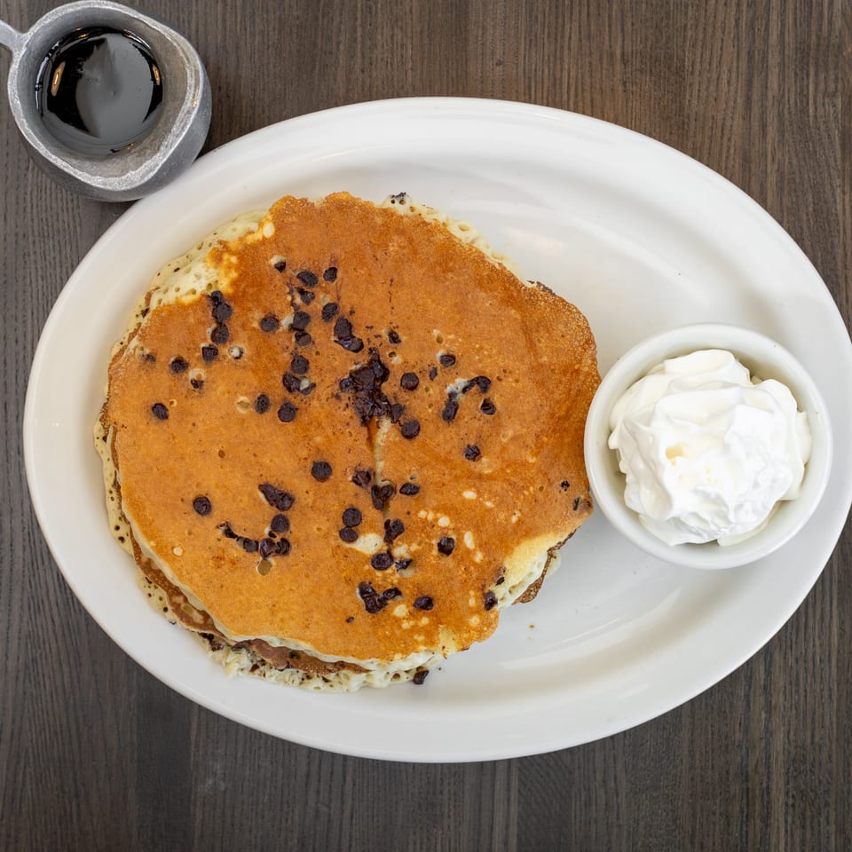 Overhead view of chocolate chip pancakes with whipped cream and a side of syrup.