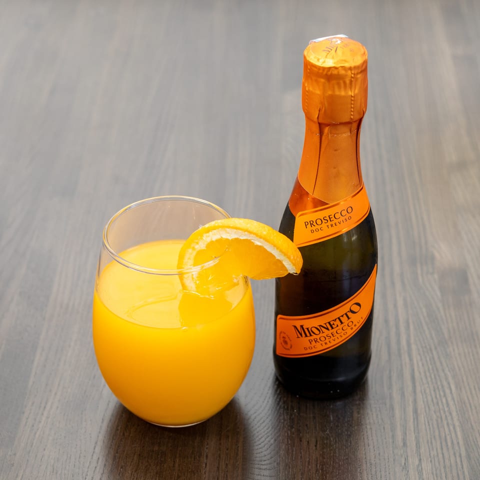 Mimosa cocktail with an orange slice next to a small bottle of Mionetto Prosecco.
