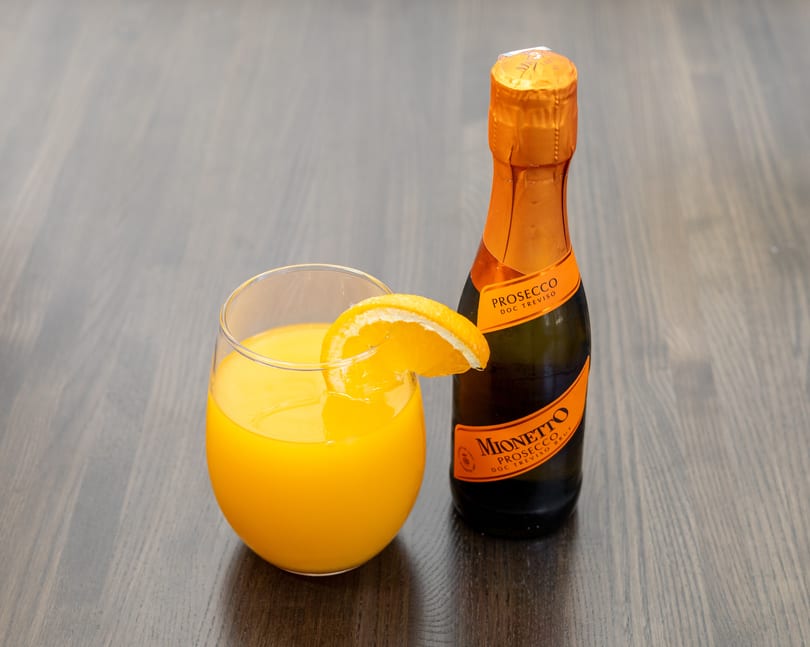 Mimosa cocktail with an orange slice next to a small bottle of Mionetto Prosecco.