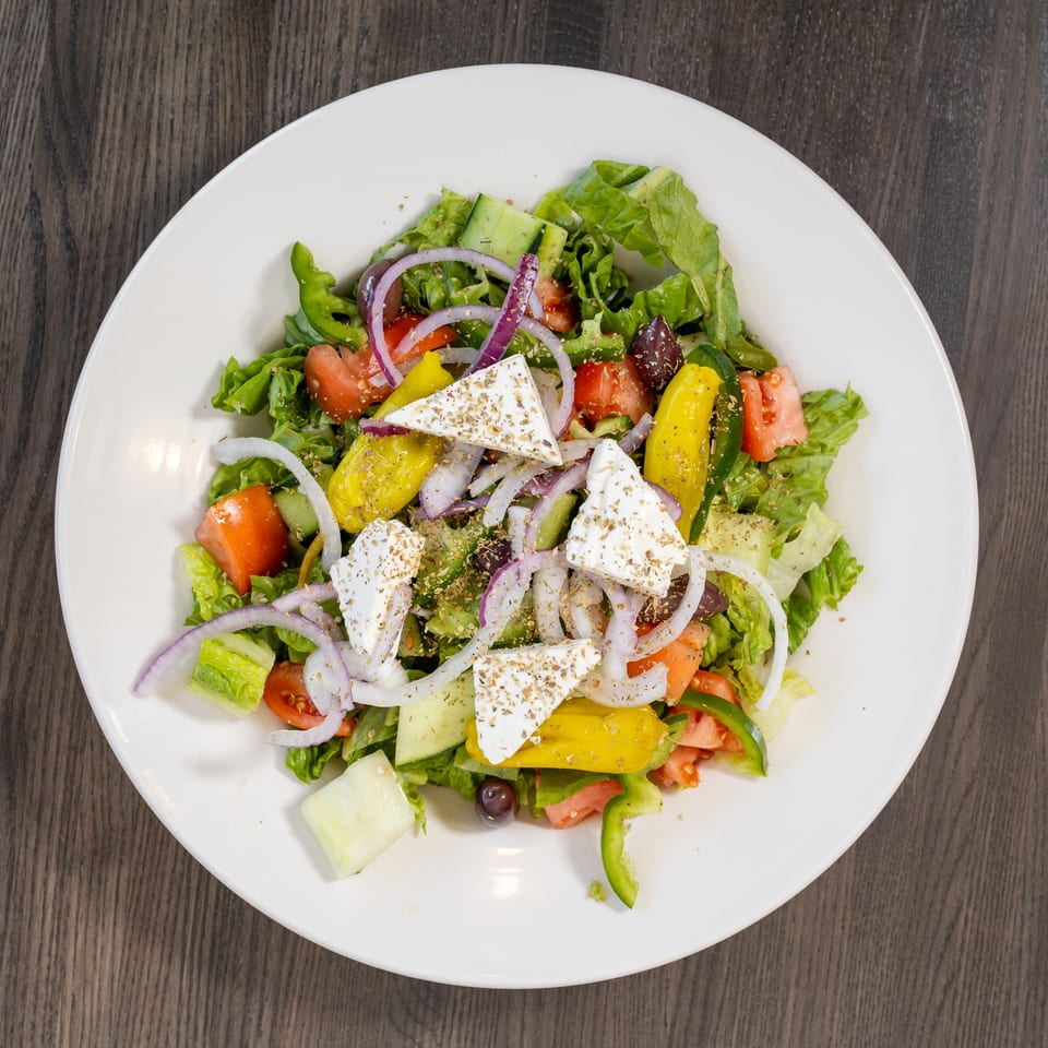 A vibrant Greek salad with lettuce, tomatoes, cucumbers, onions, peppers, olives, and feta cheese.