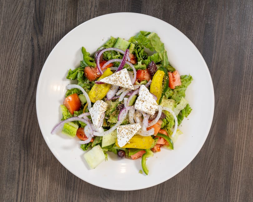 A vibrant Greek salad with lettuce, tomatoes, cucumbers, onions, peppers, olives, and feta cheese.