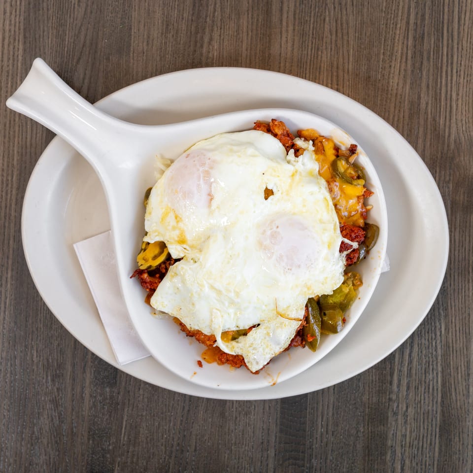 Breakfast skillet with two fried eggs, chorizo, melted cheese, and green peppers on a wooden table.