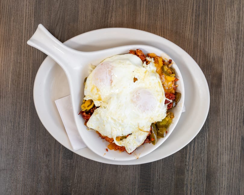 Breakfast skillet with two fried eggs, chorizo, melted cheese, and green peppers on a wooden table.