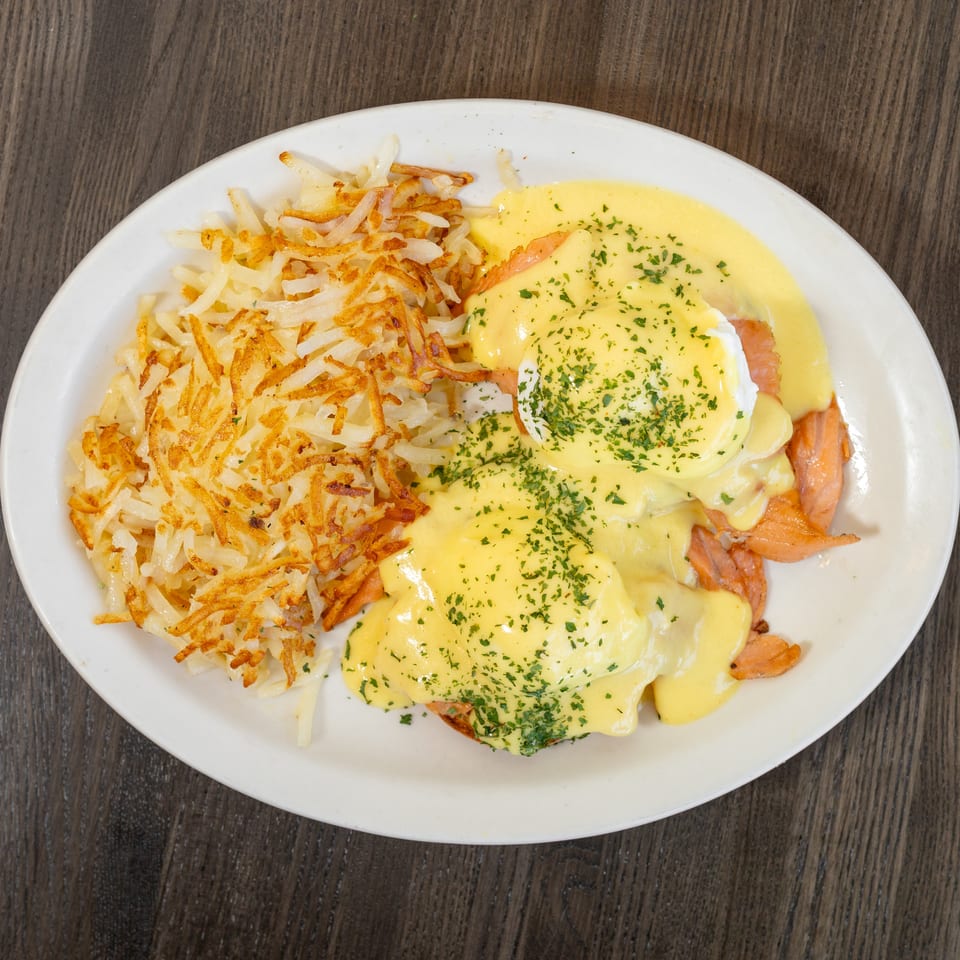 Eggs Benedict with smoked salmon and hollandaise sauce, served with crispy hash browns on a white plate.