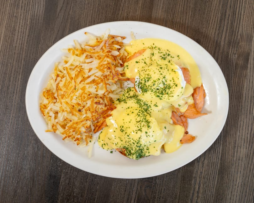 Eggs Benedict with smoked salmon and hollandaise sauce, served with crispy hash browns on a white plate.